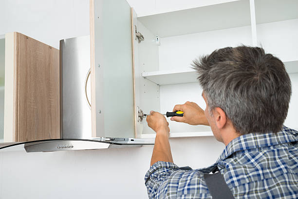 Rear view of serviceman fixing cabinet with screwdriver in kitchen